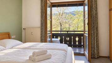 Ein Hotelzimmer mit Bett, einem Fenster mit Vorhängen, einem Heizkörper und Blick auf Bäume und Berge.