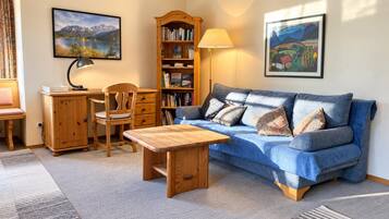 Ein gemütliches Wohnzimmer mit einem blauen Sofa, einem Holztisch und einem Bücherregal.
