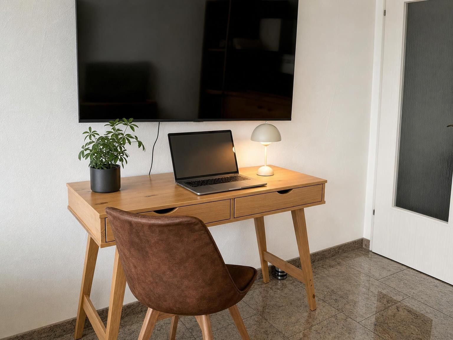 Ein Arbeitsplatz mit einem Laptop, einer Schreibtischlampe und einer Topfpflanze.