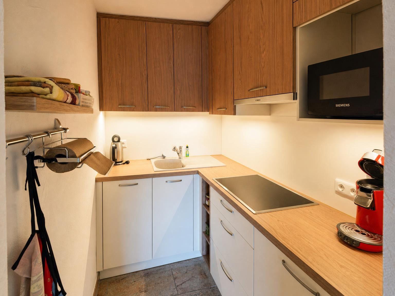 A compact kitchen with wooden cabinets, a stainless steel sink, a built-in oven, and a red coffee maker.