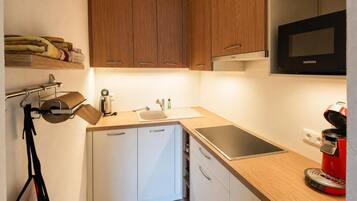 A compact kitchen with wooden cabinets, a stainless steel sink, a built-in oven, and a red coffee maker.