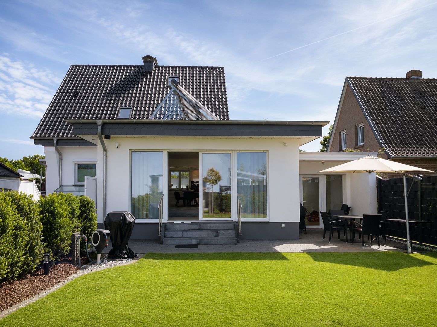 Ein modernes, zweistöckiges Haus mit überdachter Terrasse, Grill und gepflegtem Rasen.