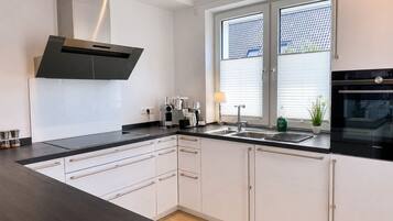 Eine moderne Küche mit eingebautem Backofen, einer Edelstahl-Dunstabzugshaube, einer Spüle mit zwei Becken und einem Fenster mit Jalousien.