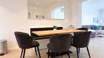 Uma sala de jantar moderna com mesa de madeira, quatro cadeiras estofadas, uma pequena planta em vaso e um abajur branco.