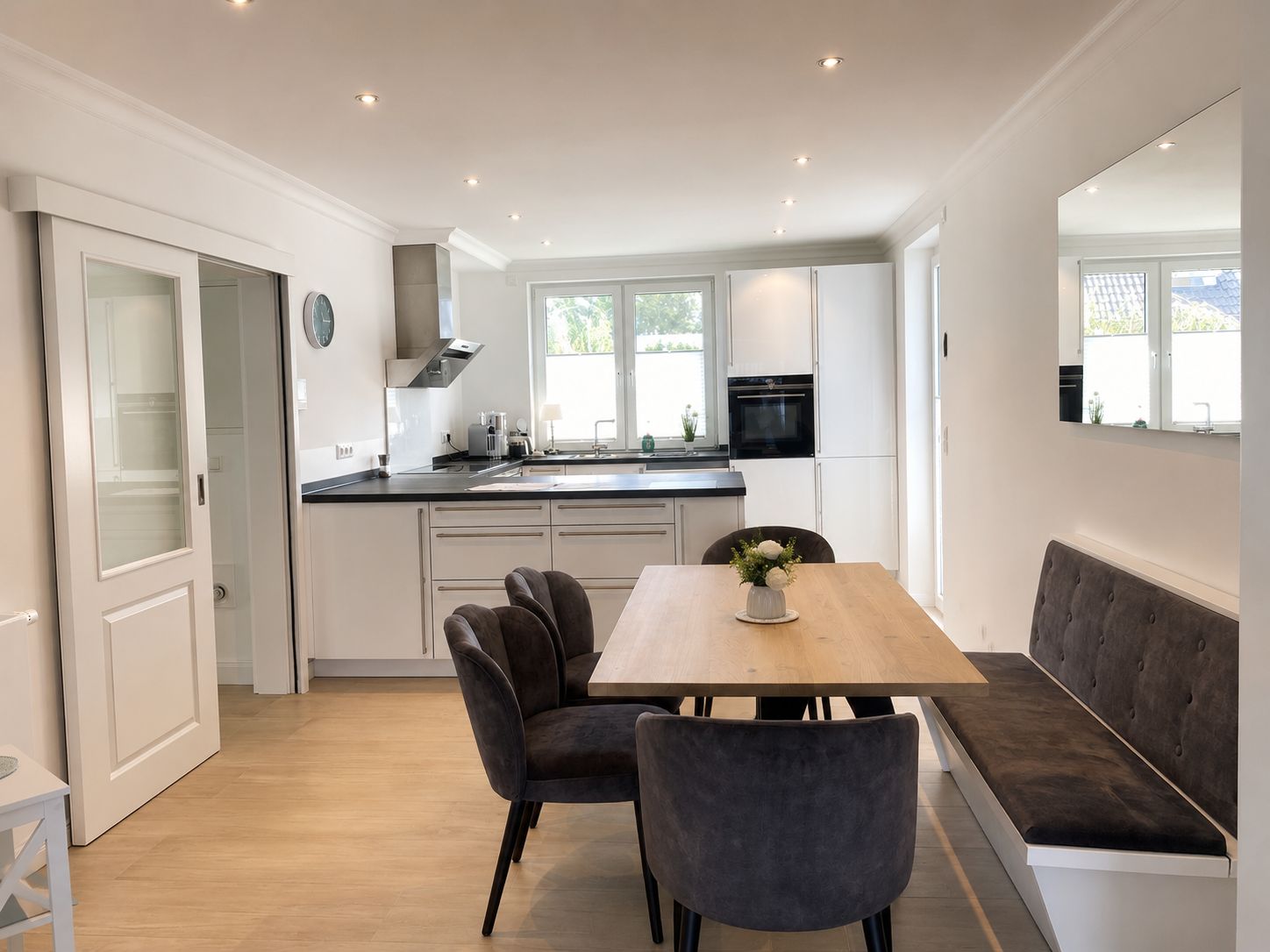A modern kitchen with white cabinets, a black oven, and a dining area with a wooden table and two chairs.