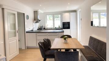A modern kitchen with white cabinets, a black oven, and a dining area with a wooden table and two chairs.