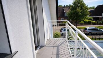 Un balcone con ringhiera bianca, vista libera su una strada residenziale e un'auto parcheggiata.