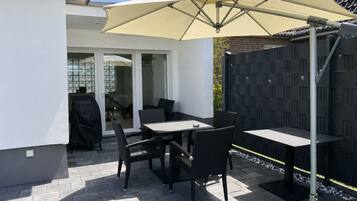 An outdoor patio with a table and chairs, a large umbrella, and a view of a house through glass doors.