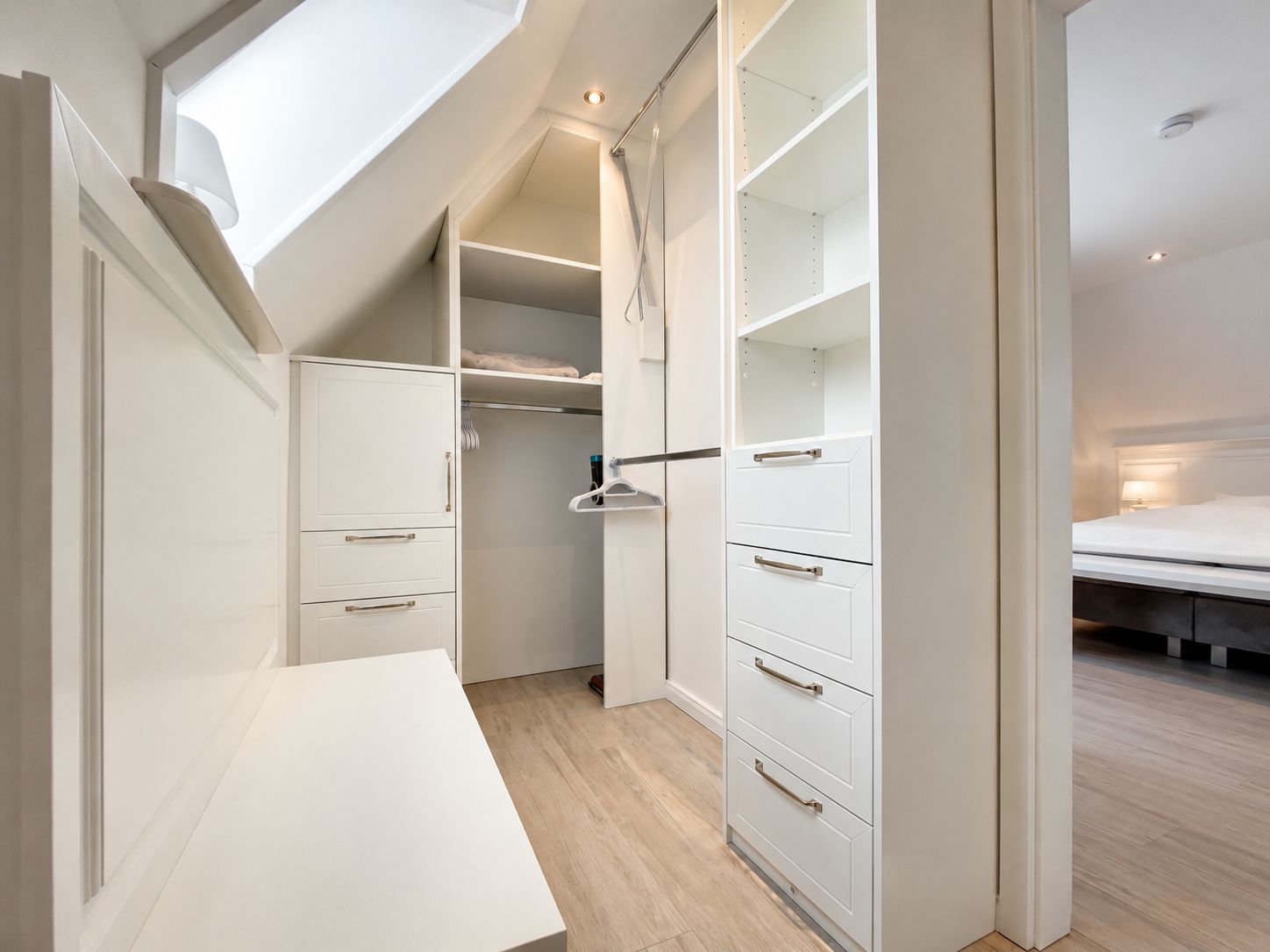 A modern bedroom with a skylight, a white bed, and a built-in wardrobe.