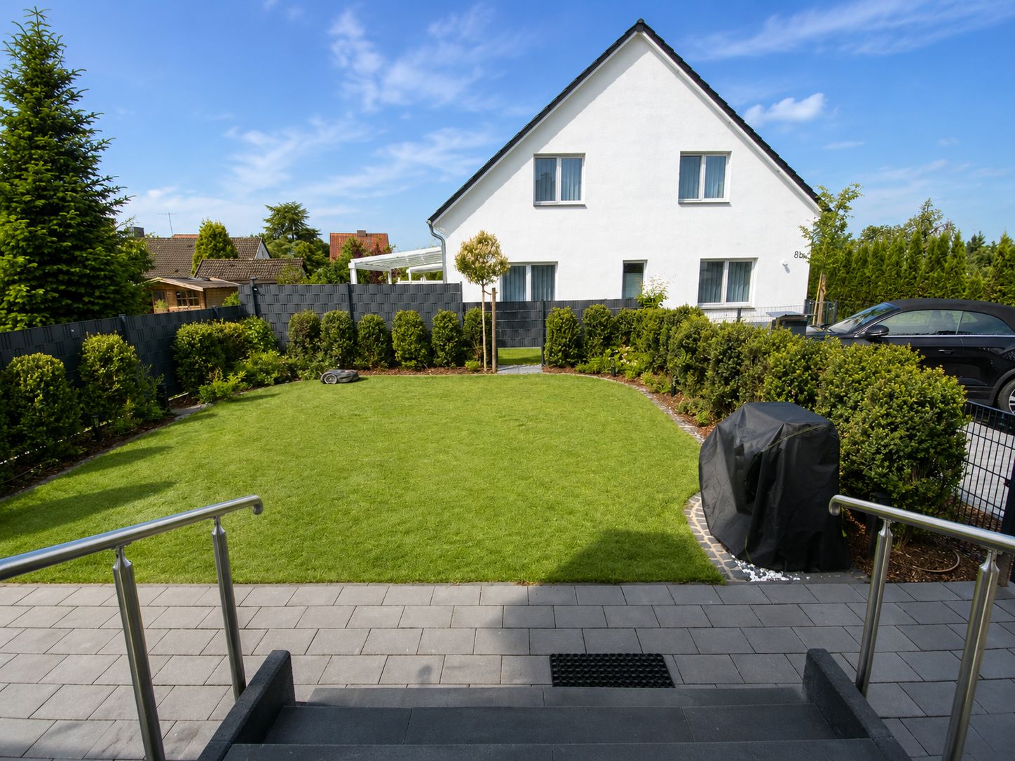 A residential property with a well-maintained lawn, a covered outdoor seating area, and a staircase leading to the entrance.
