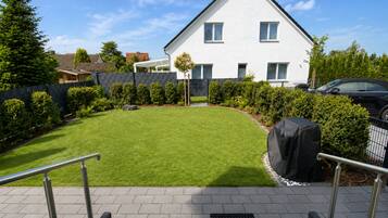 A residential property with a well-maintained lawn, a covered outdoor seating area, and a staircase leading to the entrance.