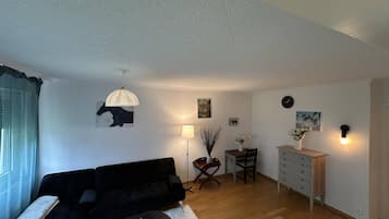 A living room with a black sofa, a small round coffee table, a floor lamp, a dining table with chairs, and a cabinet.