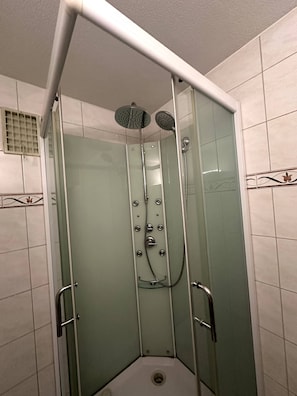 Une cabine de douche fermée par des parois en verre, dotée d’un pommeau de douche à main et d’un robinet mural.