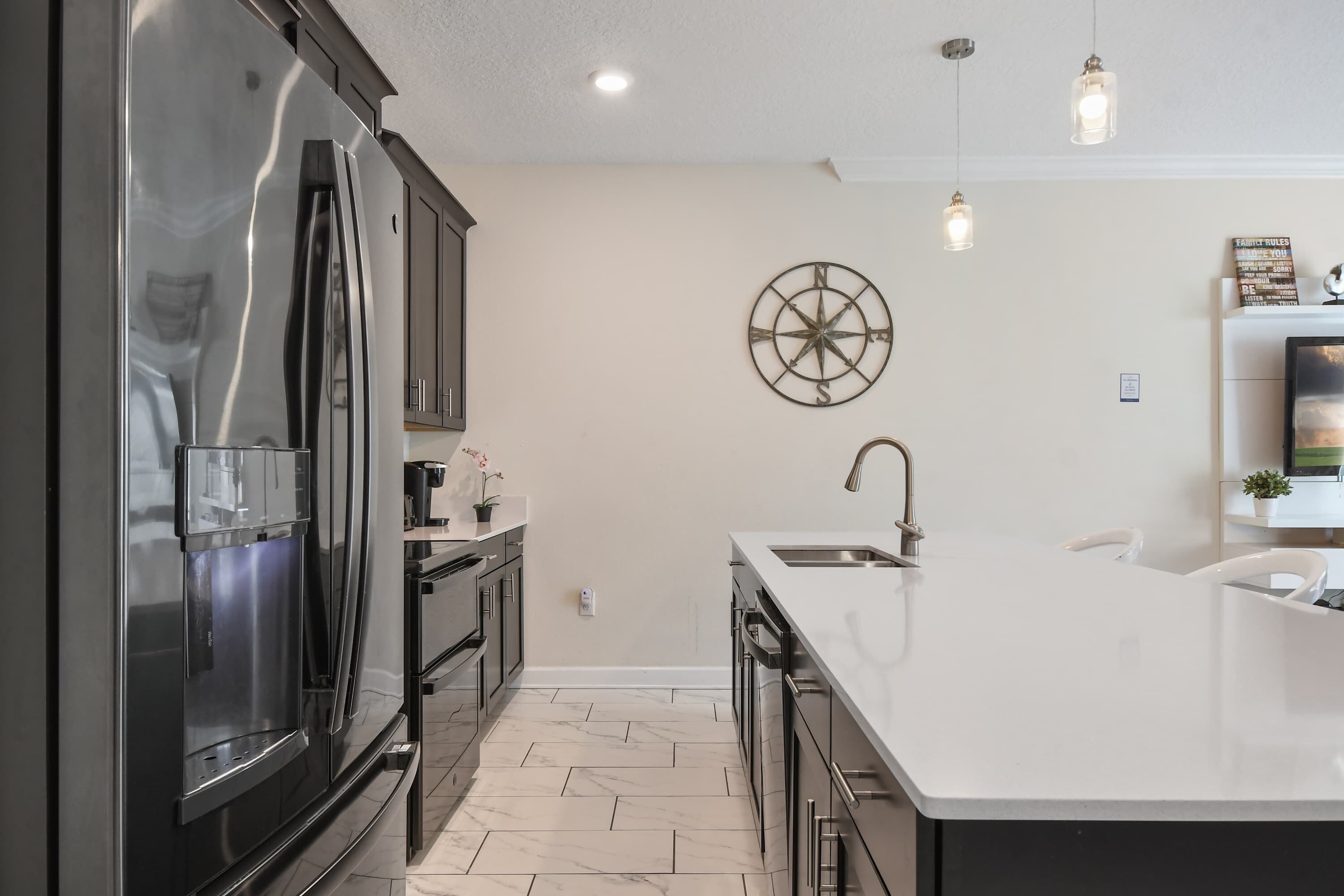 A modern kitchen with a large island, stainless steel appliances, and a decorative compass wall art.