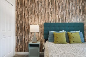 A bedroom with a wooden wall panel, a bed with multiple pillows, a bedside table with a lamp, and a power outlet. - ChampionsGate Townhome w/ Private Pool (Kissimmee)