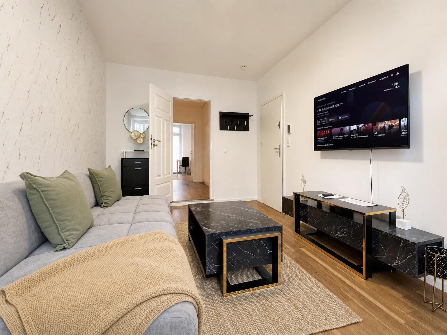 Ein modernes Wohnzimmer mit einer Couch, einem Couchtisch und einem an der Wand befestigten Fernseher.