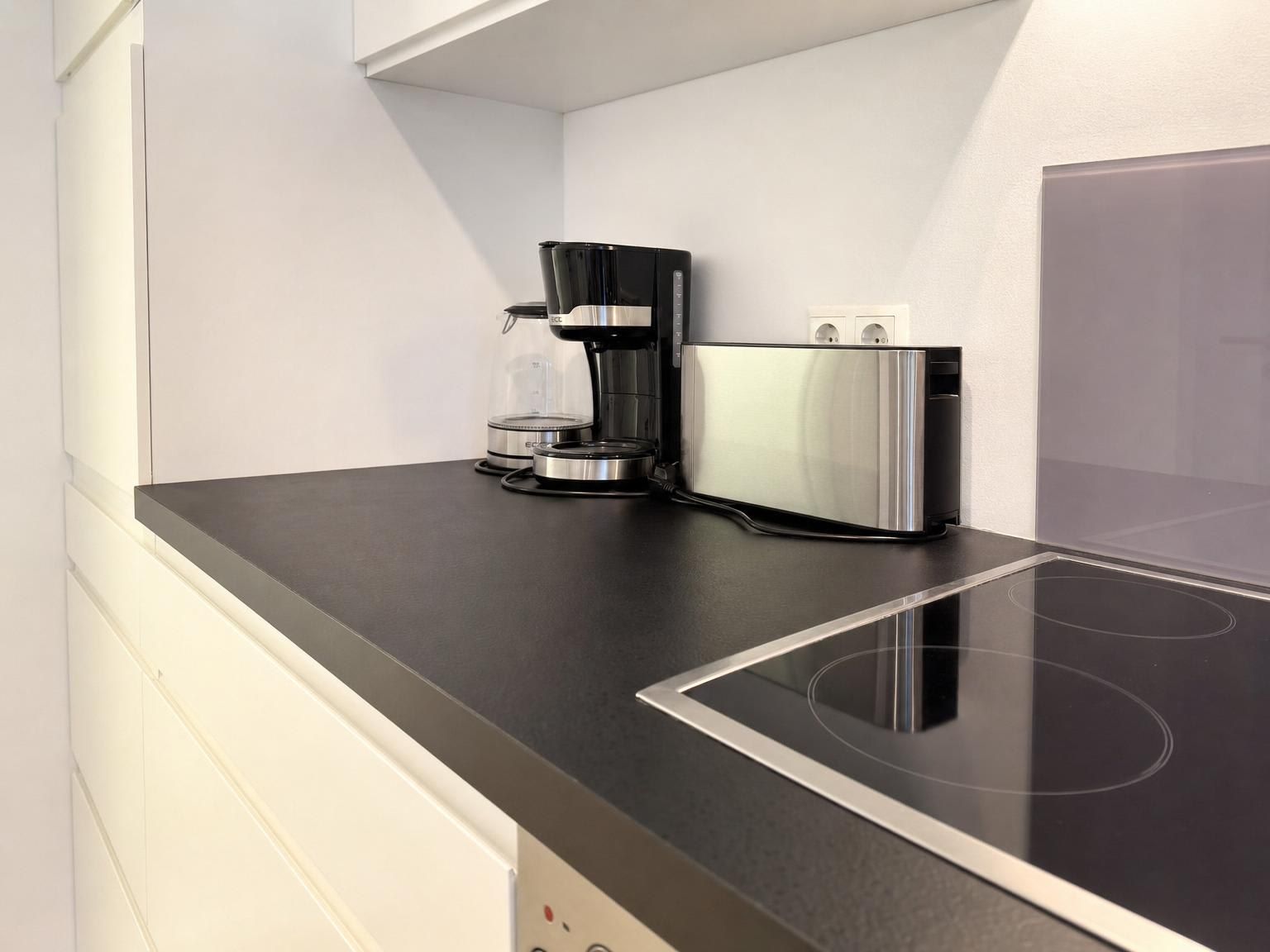 A modern kitchen with a black countertop, a coffee maker, and a stainless steel appliance.