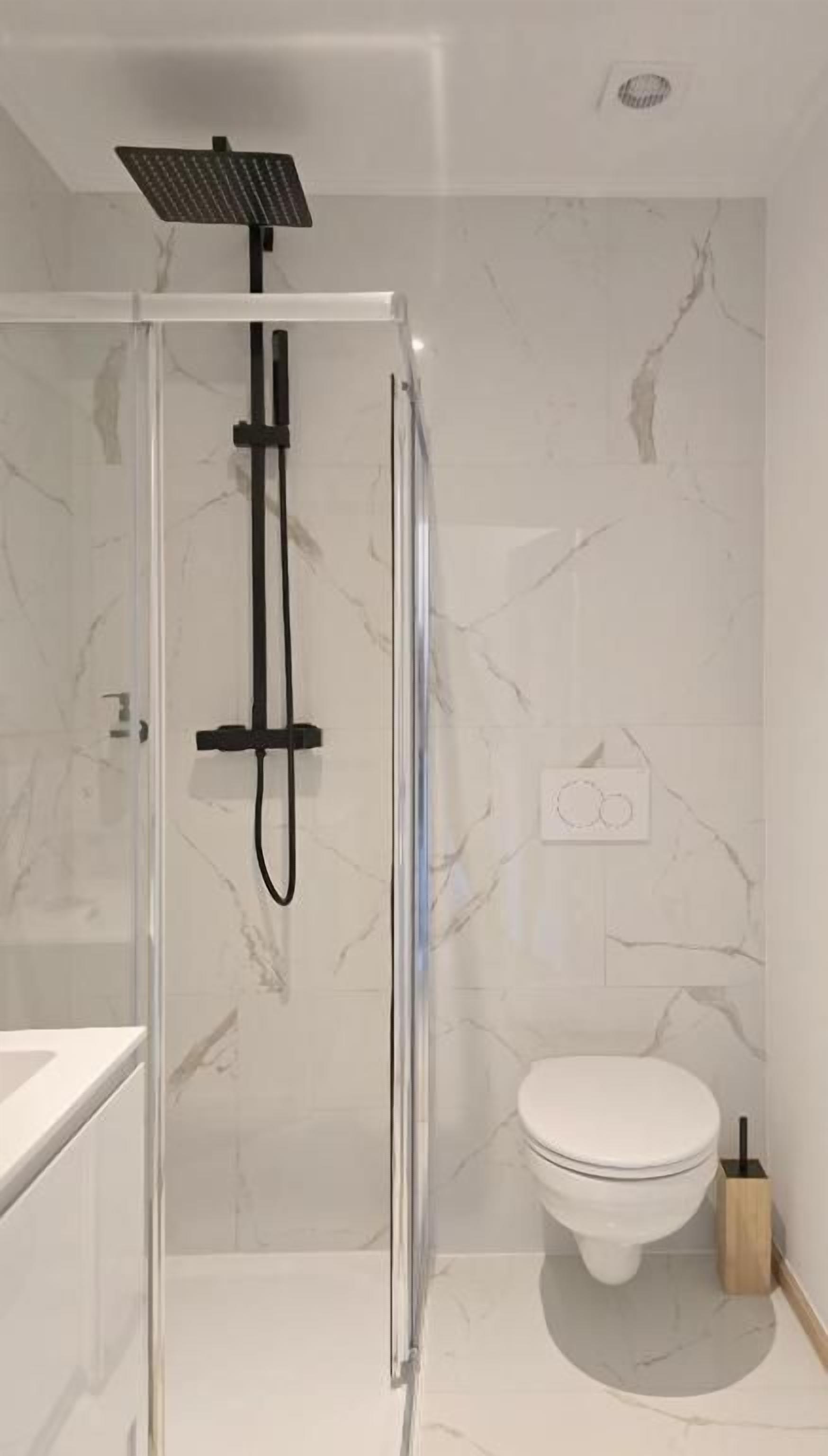 A modern bathroom with a glass-enclosed shower, a white toilet, and marble tiles.