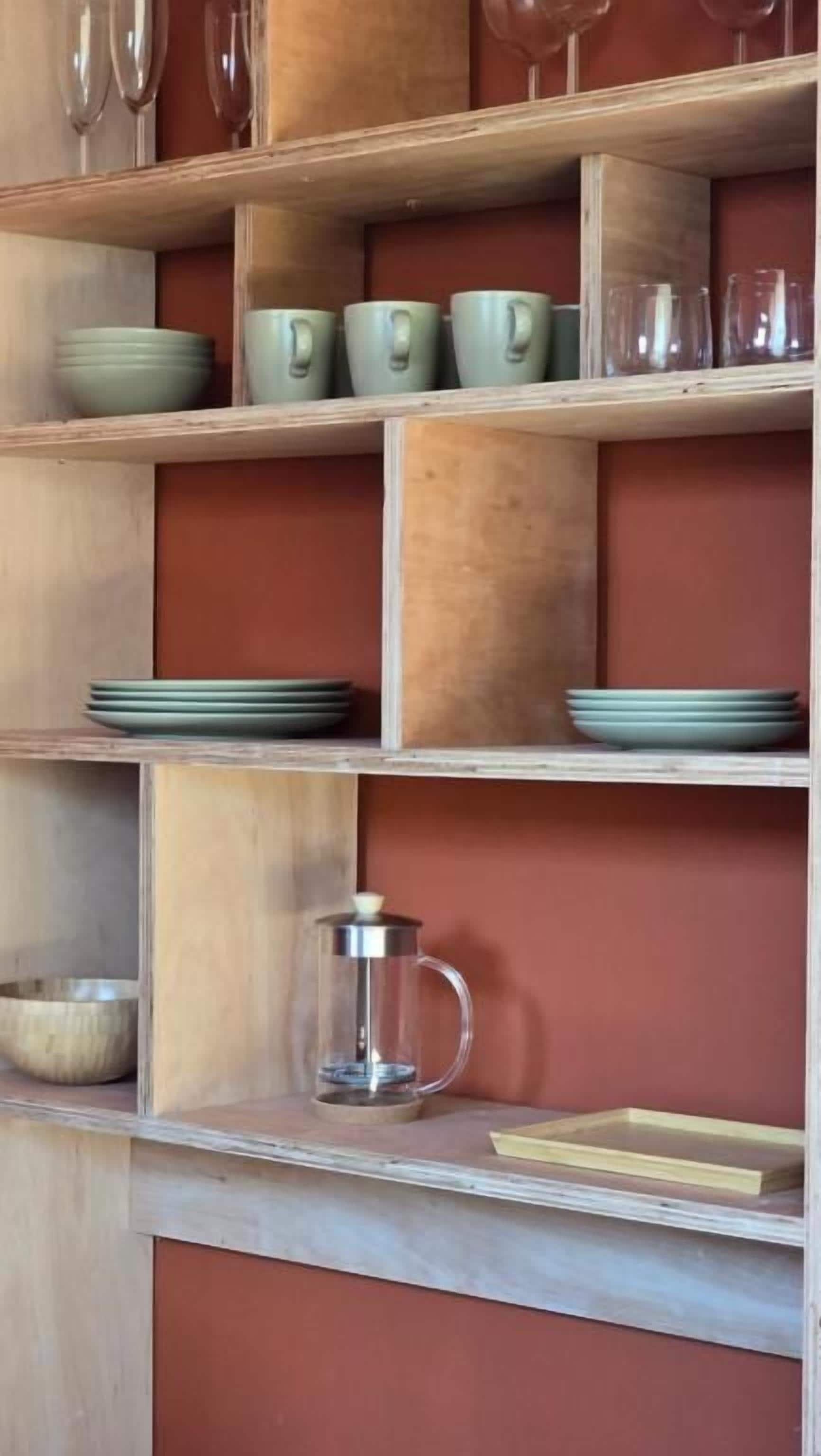 A wooden shelf with various kitchenware including plates, cups, and a coffee pot.