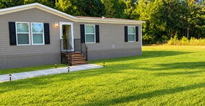 Une maison mobile de plain-pied, dotée d’un porche à l’avant, d’un escalier menant à l’entrée et d’une pelouse bien entretenue.