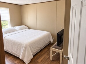 A bedroom with a bed, a television on a small table, and a door. - Foley Retreat | 4 Bedrooms • Grill & Smoker (Foley)