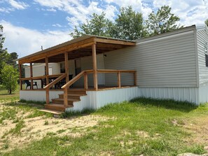 A single-story mobile home with a wooden porch and a staircase leading to an upper level.