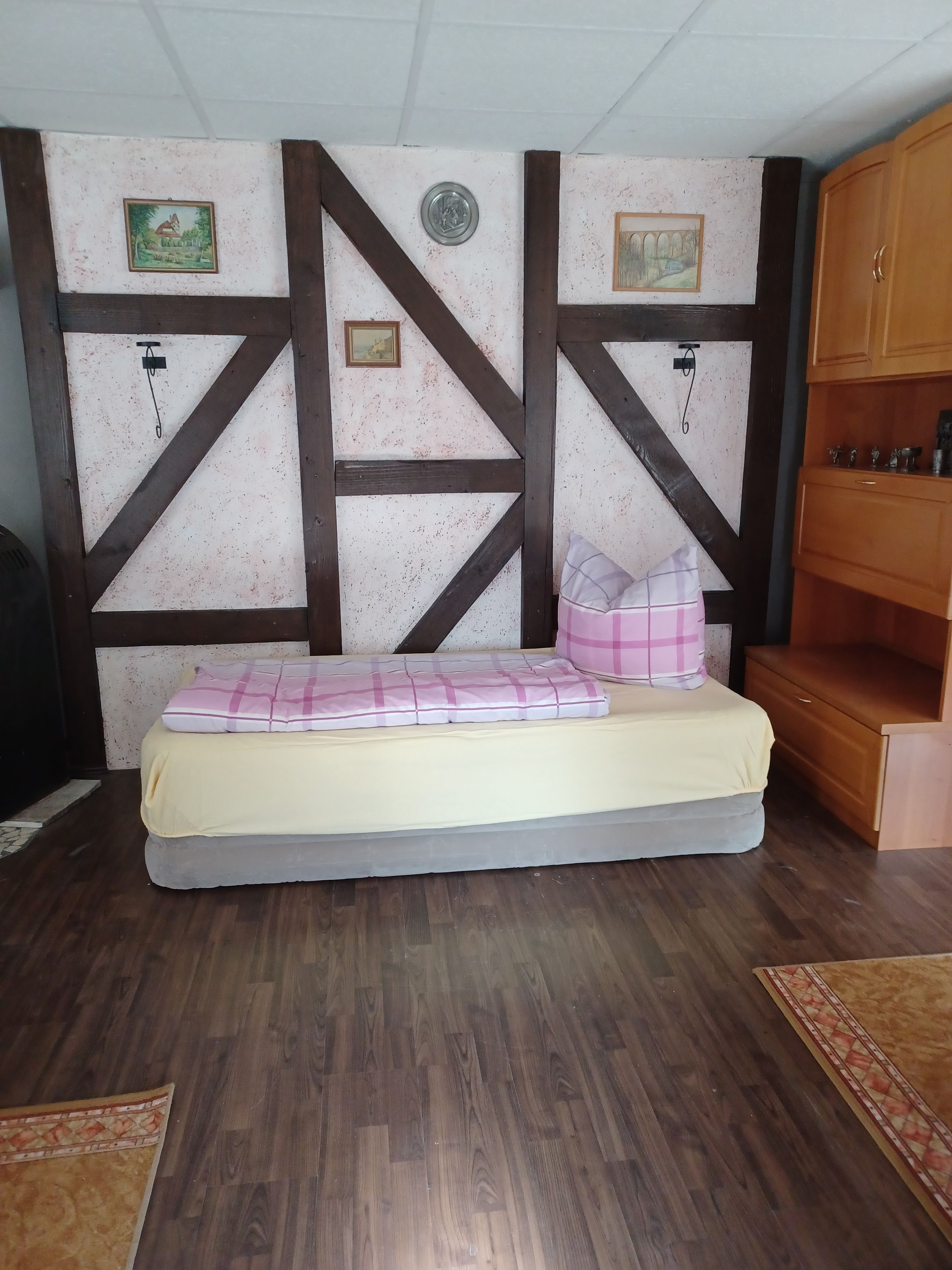 Ein Zimmer mit einem Bett, einem hölzernen Kleiderschrank und einer Wand mit dekorativem Muster.
