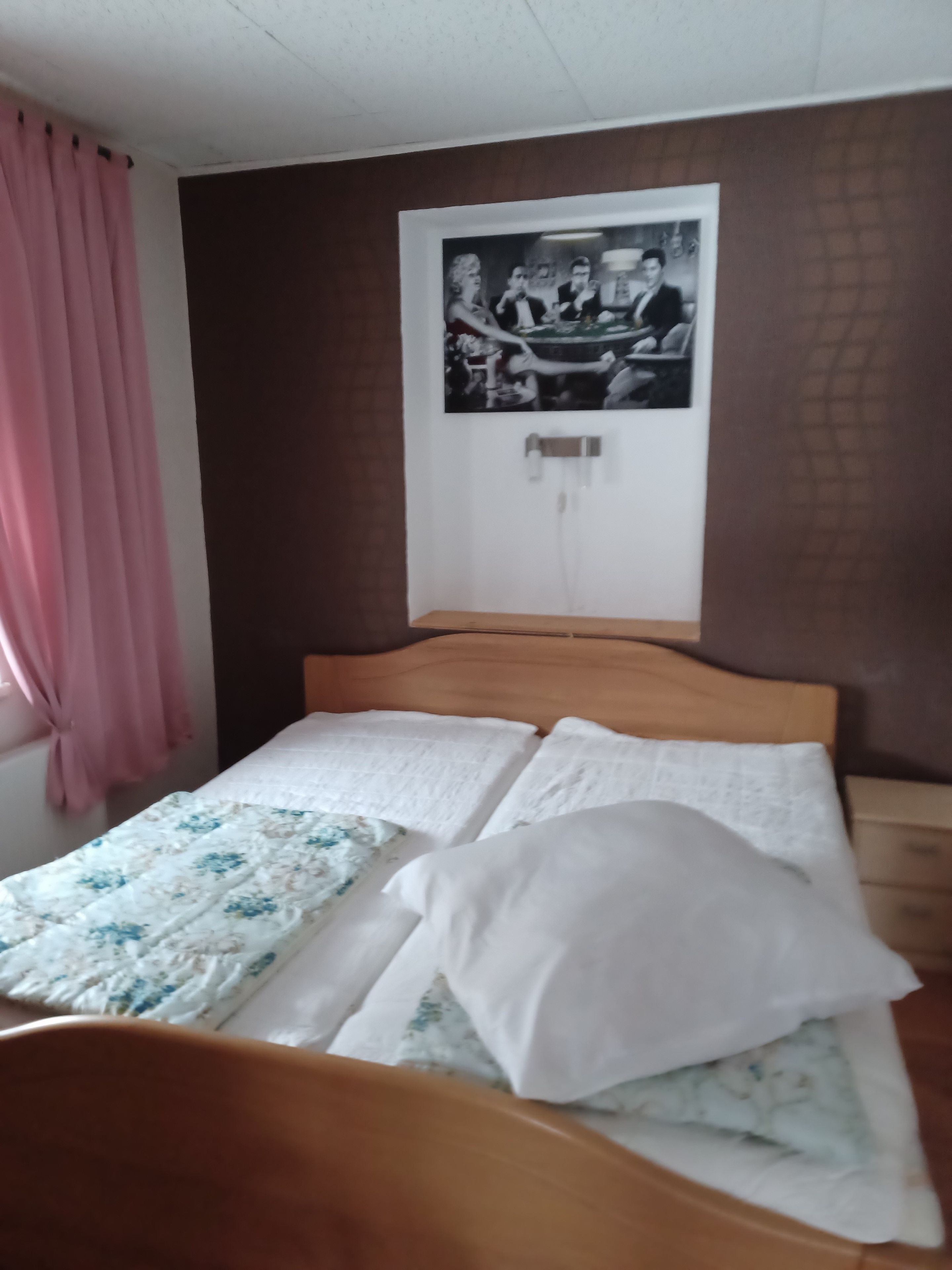 Ein Zimmer mit einem Bett, einem gerahmten Bild an der Wand und einem Fenster mit Vorhängen.