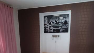 Ein Zimmer mit einem Bett, einem gerahmten Bild an der Wand und einem Fenster mit Vorhängen.