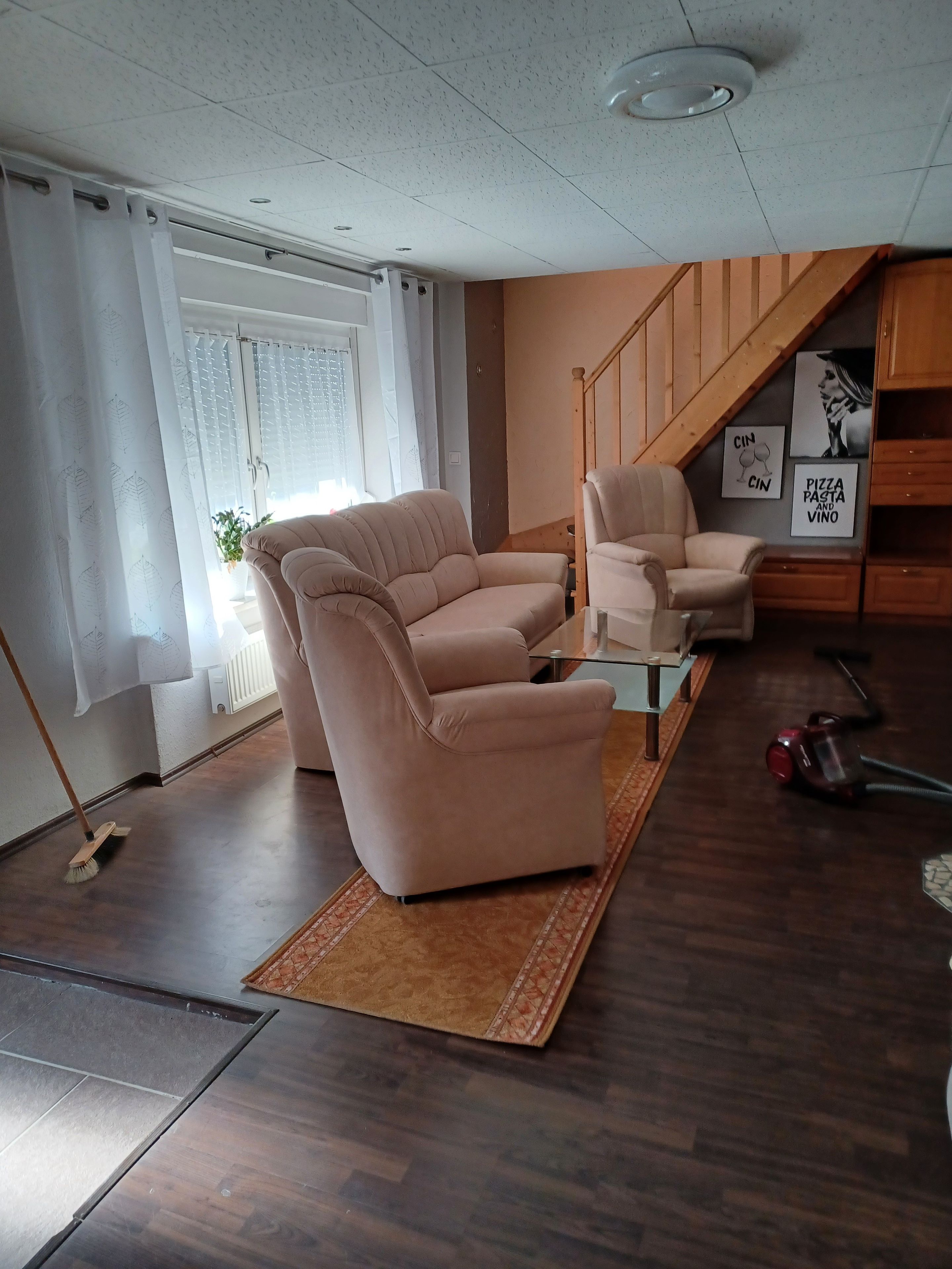 Ein Wohnzimmer mit einer Couch, Sesseln, einem Couchtisch und einem Staubsauger.