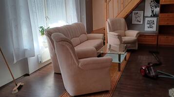 Ein Wohnzimmer mit einer Couch, Sesseln, einem Couchtisch und einem Staubsauger.