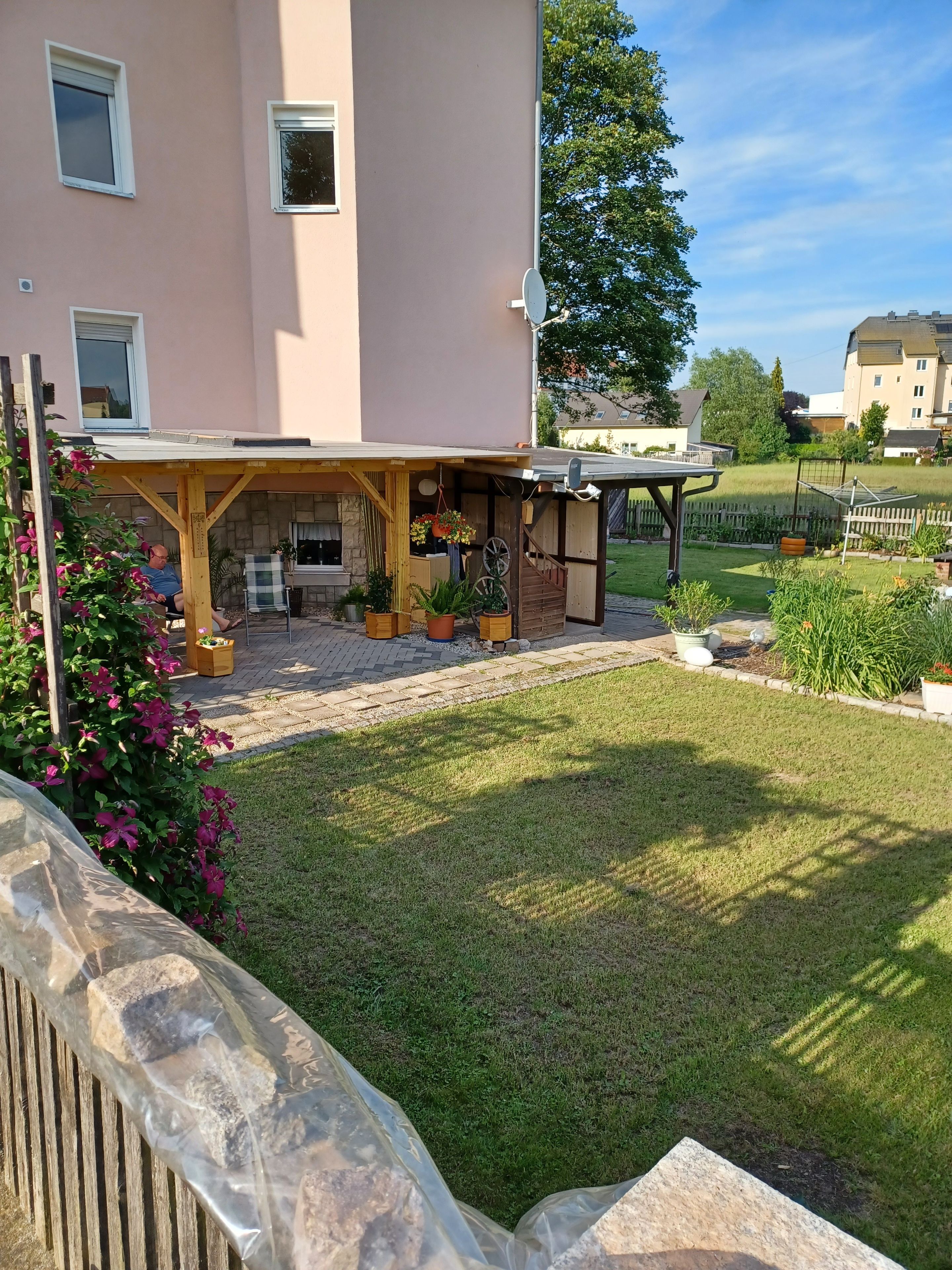 A residential building with a covered patio area, a stone wall, and a well-maintained lawn.