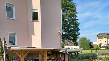 A residential building with a covered patio area, a stone wall, and a well-maintained lawn.