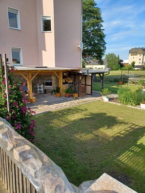 A residential building with a covered patio area, a stone wall, and a well-maintained lawn. - Apartment 'Ferienwohnung Ursula Rudolph' with Shared Terrace, Shared Garden and Wi-Fi (Gersdorf)