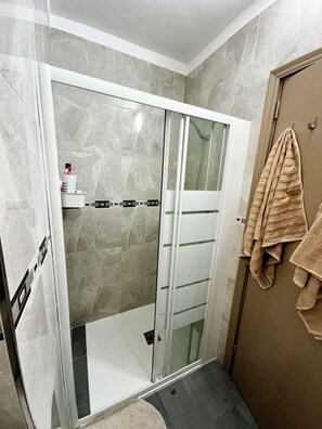 A bathroom with a glass-enclosed shower, a towel rack with towels, and a marble wall. - Great 2BR Apartment with 4 min walk everywhere (Playa San Juan)