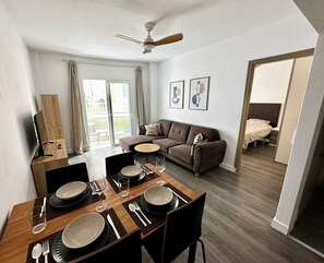 A modern living room with a dining area, a ceiling fan, a sofa, and a view of the outdoors. - Great 2BR Apartment with 4 min walk everywhere (Playa San Juan)