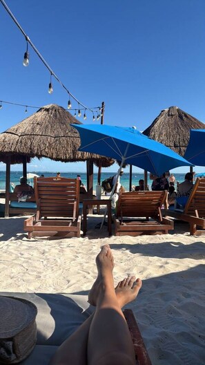 Eine Strandansicht mit Holzliegen und Reetdachschirmen.