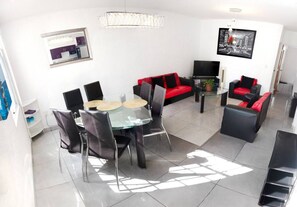Ein modernes Wohnzimmer mit einem Glastisch, schwarzen und roten Sofas, einem Flachbildfernseher und einem Gemälde an der Wand.