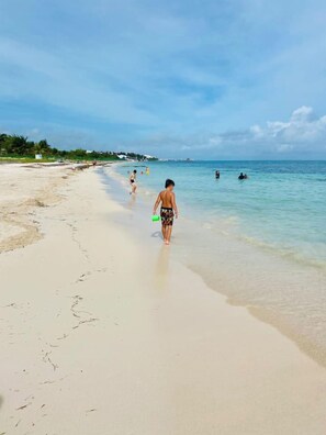 A beach with a clear sky, calm sea, and people walking along the shore. - Casa Inn Retreat | Villas Morelos II (Puerto Morelos)