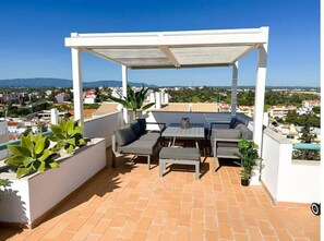 Eine Dachterrasse mit überdachter Sitzgelegenheit, einem Tisch und Topfpflanzen.