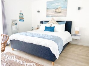 A bedroom with a bed, a chair, a nightstand, a lamp, and a wall decoration. - Carvoeiro Beach House (Carvoeiro)