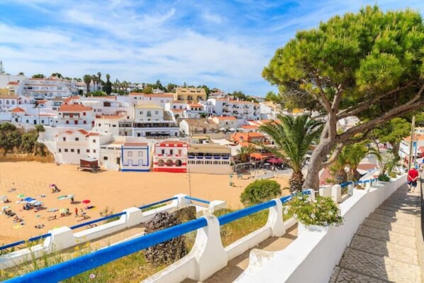 Un pueblo costero con edificios blancos, una playa arenosa y una barandilla azul.
