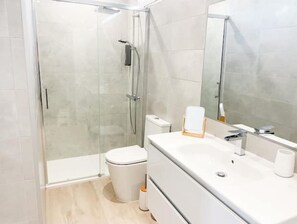 Un baño moderno con cabina de ducha de vidrio, inodoro blanco y tocador con espejo.
