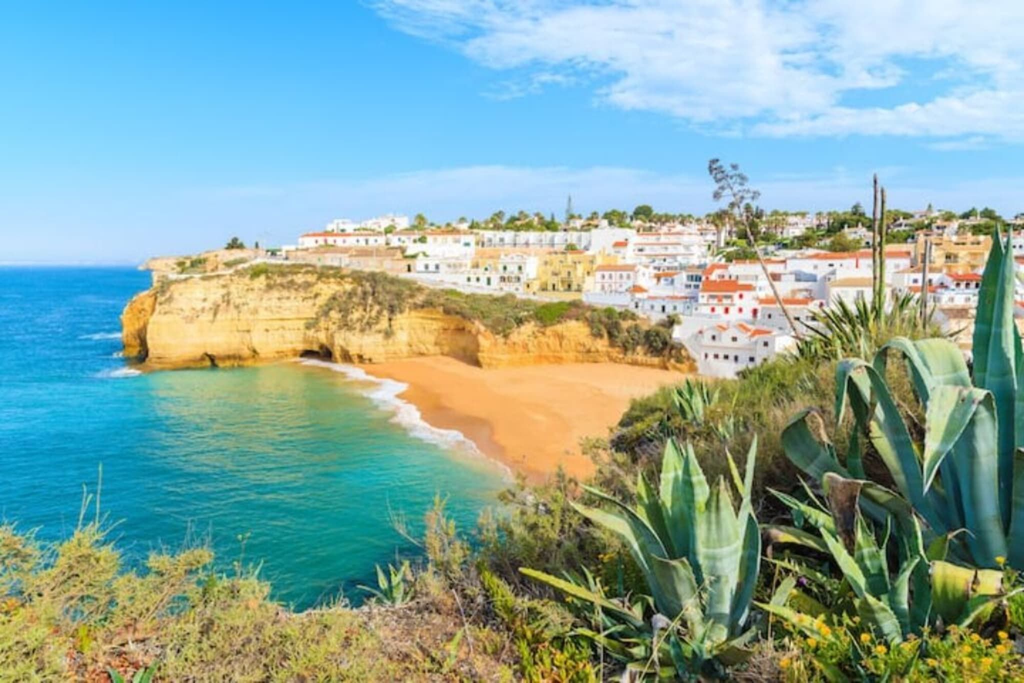 A coastal town with buildings along the cliffside, a sandy beach, and clear blue sea.