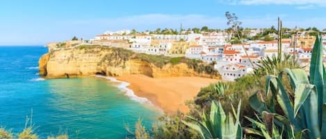 A coastal town with buildings along the cliffside, a sandy beach, and clear blue sea.