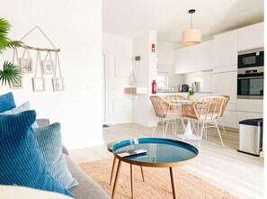 Ein modernes Wohnzimmer mit einem Glastisch, einer blauen Sitzsofa und einem Essbereich mit Korbstühlen.