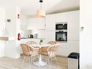 A modern kitchen with white cabinetry, a round dining table with wicker chairs, and built-in appliances. - Carvoeiro Beach House (Carvoeiro)