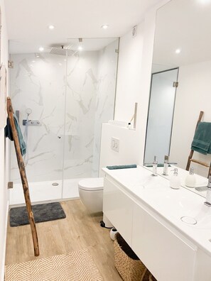 A modern bathroom with a glass shower enclosure, a white toilet, and a vanity with a mirror. - Casa Eden (Ferragudo)