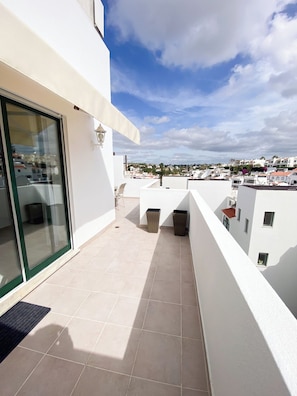 A balcony with a glass door, tiled floor, and a view of a residential area. - Casa Joao (Carvoeiro)