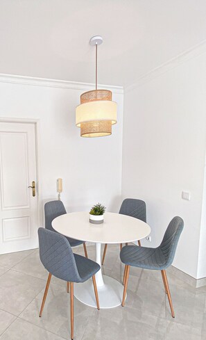 A round table with four chairs, a hanging light fixture, and a small plant on the table. - Casa Joao (Carvoeiro)